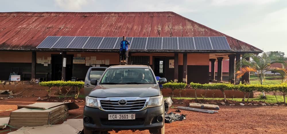 A technician standing on a ladder in front of solar panels installed on the roof of a school building