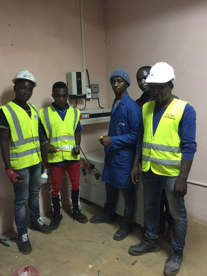 A team in hard hats and safety vests beside the inverter system they installed