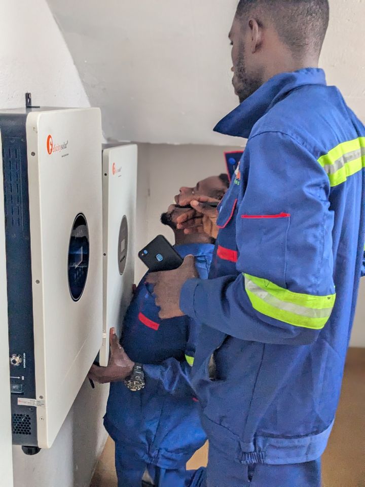 Two technicians mounting and checking a hybrid inverter on a wall