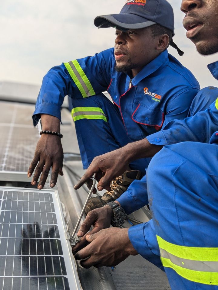 Two technicians in SmartSana Energies overalls fixing a solar module clamp on a roof