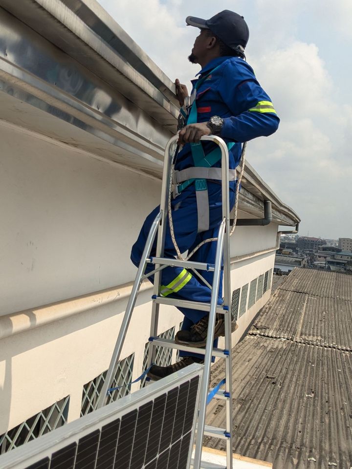 A technician in a safety harness on a stepladder, inspecting a roof edge before installing panels